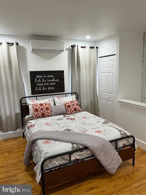 bedroom with hardwood / wood-style floors, an AC wall unit, and a closet