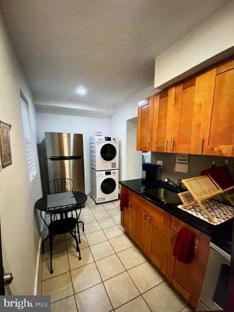 kitchen featuring light tile patterned flooring, stainless steel fridge, stacked washer and clothes dryer, and sink