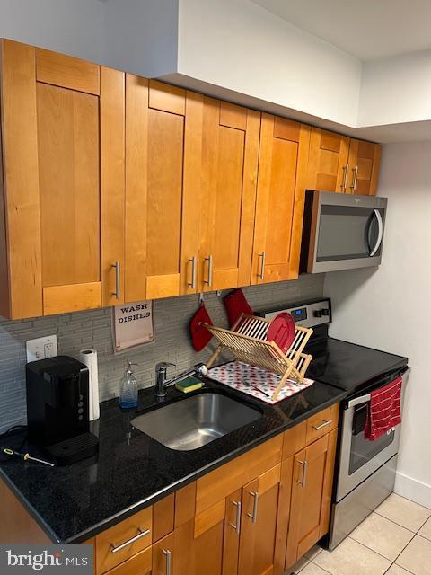 kitchen featuring backsplash, sink, dark stone countertops, light tile patterned floors, and appliances with stainless steel finishes