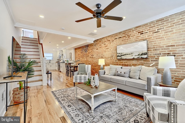 living room with light hardwood / wood-style flooring, ceiling fan, crown molding, and brick wall