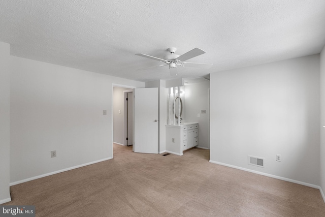 unfurnished bedroom with ensuite bath, ceiling fan, light carpet, and a textured ceiling