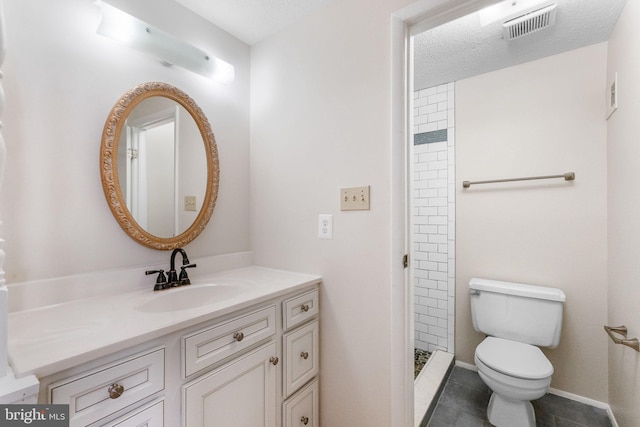 bathroom with a tile shower, vanity, a textured ceiling, and toilet