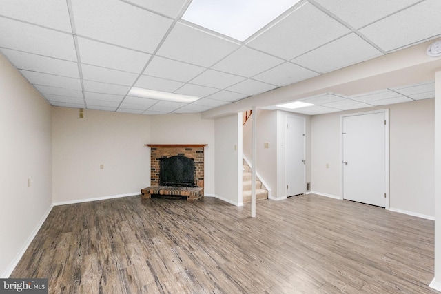 basement with a drop ceiling, hardwood / wood-style floors, and a brick fireplace