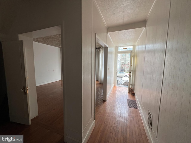 corridor with hardwood / wood-style floors, wood walls, and a textured ceiling