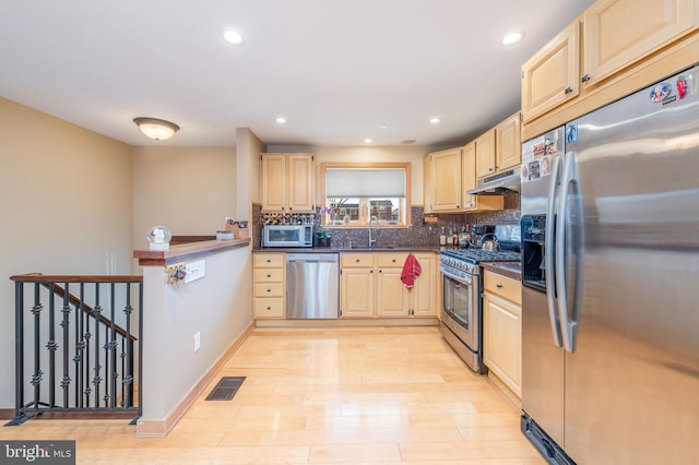 kitchen with sink, light brown cabinets, stainless steel appliances, decorative backsplash, and light wood-type flooring