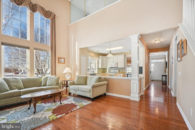 living room featuring dark wood-type flooring, a high ceiling, and ornate columns