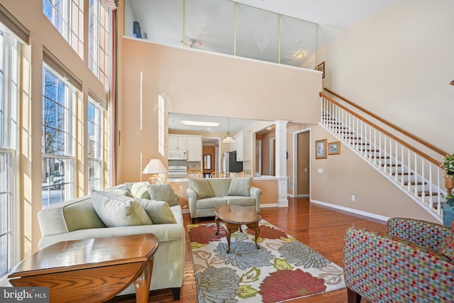 living room with ceiling fan, dark wood-type flooring, a high ceiling, and decorative columns