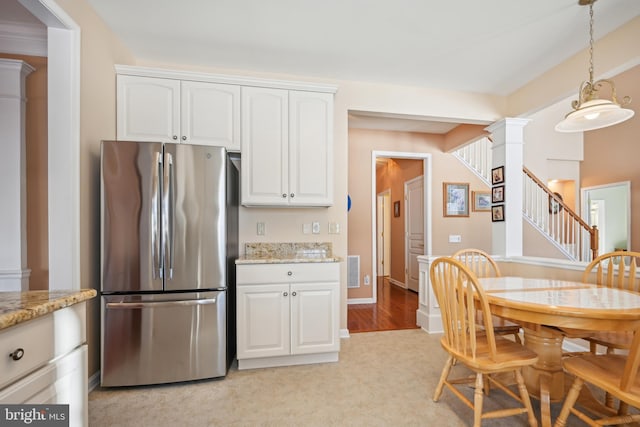 kitchen featuring stainless steel refrigerator, light stone counters, white cabinetry, and decorative columns