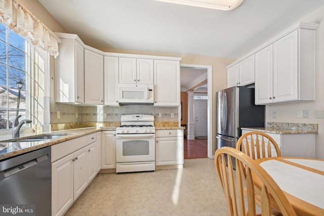 kitchen featuring light stone countertops, sink, white cabinets, and white appliances