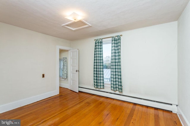 empty room featuring hardwood / wood-style flooring and a baseboard heating unit