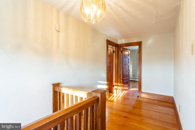 hallway with wood-type flooring, a baseboard radiator, and a notable chandelier