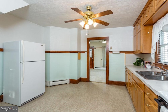 kitchen with a textured ceiling, baseboard heating, ceiling fan, sink, and white fridge