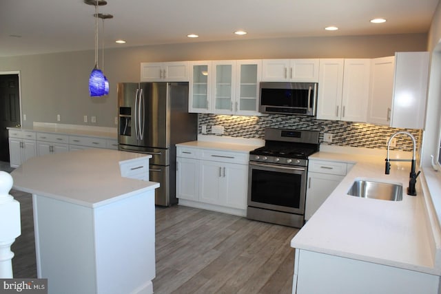 kitchen featuring white cabinetry, sink, hanging light fixtures, light hardwood / wood-style floors, and appliances with stainless steel finishes