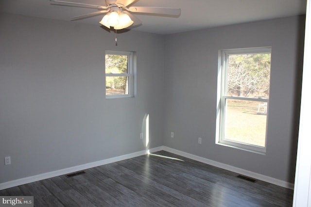 empty room with a wealth of natural light, dark wood-type flooring, and ceiling fan