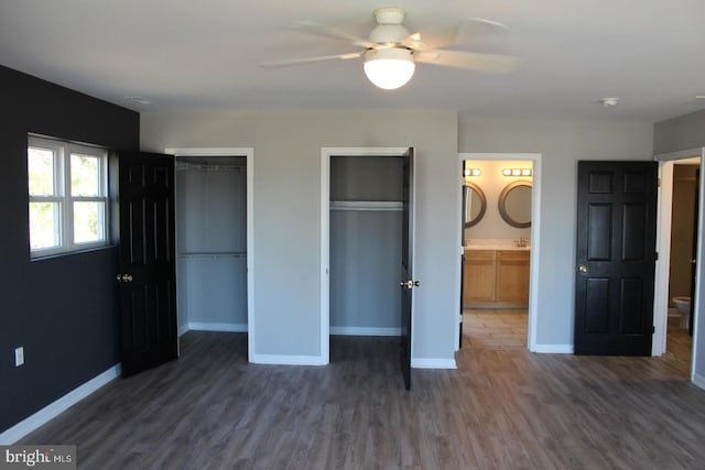 unfurnished bedroom featuring connected bathroom, two closets, ceiling fan, and dark wood-type flooring