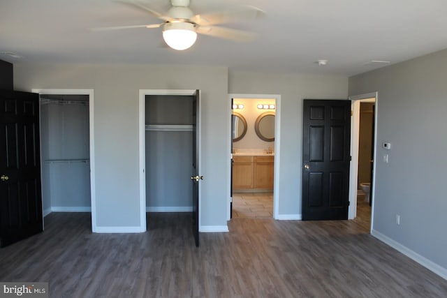 unfurnished bedroom featuring ceiling fan, dark wood-type flooring, connected bathroom, and two closets