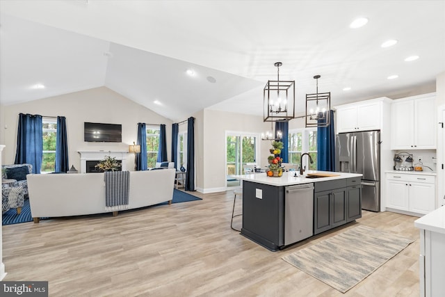 kitchen with stainless steel appliances, sink, decorative light fixtures, white cabinetry, and an island with sink