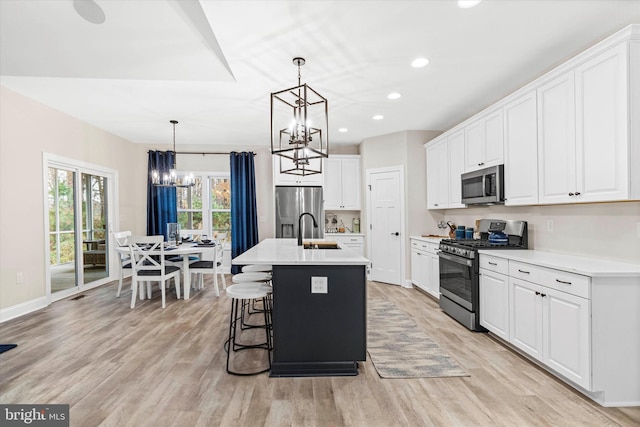 kitchen with appliances with stainless steel finishes, pendant lighting, light hardwood / wood-style flooring, white cabinets, and an island with sink