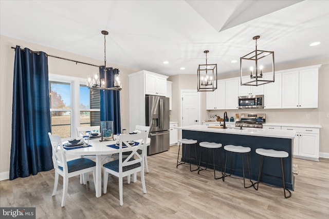 kitchen featuring white cabinetry, an island with sink, light hardwood / wood-style floors, pendant lighting, and appliances with stainless steel finishes