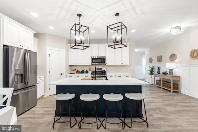 kitchen featuring decorative light fixtures, light wood-type flooring, stainless steel appliances, and a center island with sink