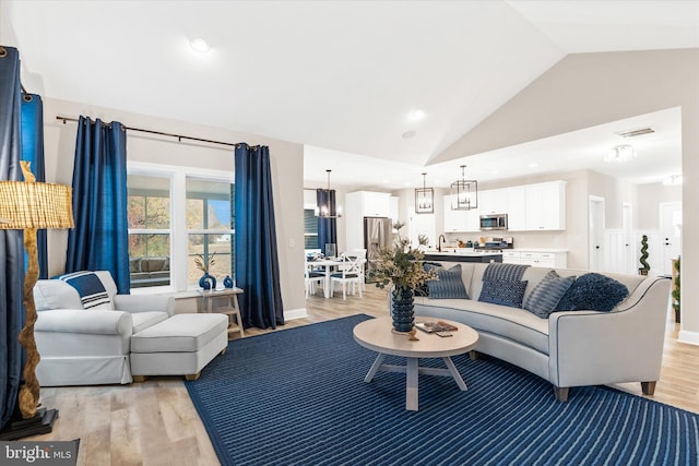 living room featuring a notable chandelier, sink, high vaulted ceiling, and light hardwood / wood-style flooring