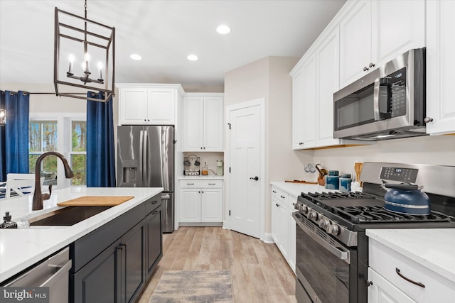 kitchen featuring pendant lighting, sink, light wood-type flooring, white cabinetry, and stainless steel appliances