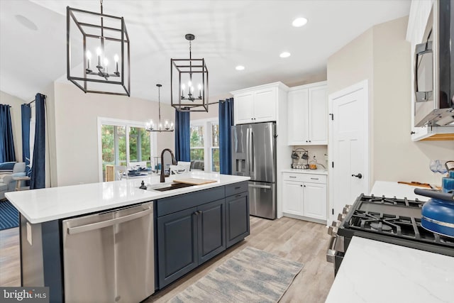 kitchen with appliances with stainless steel finishes, light wood-type flooring, sink, pendant lighting, and white cabinets