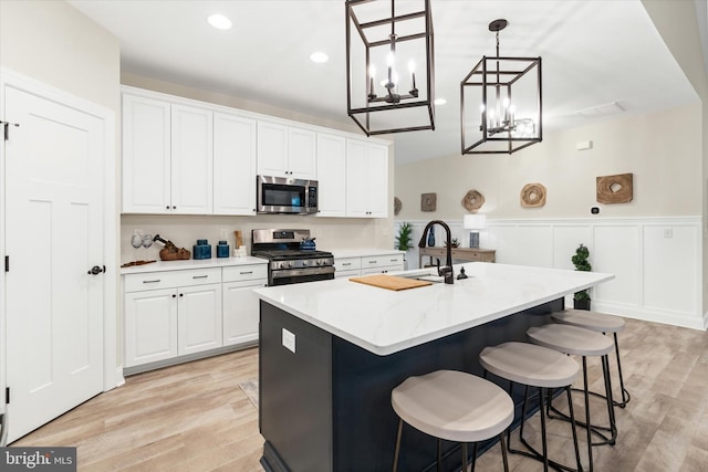 kitchen featuring a kitchen island with sink, hanging light fixtures, light wood-type flooring, white cabinetry, and stainless steel appliances