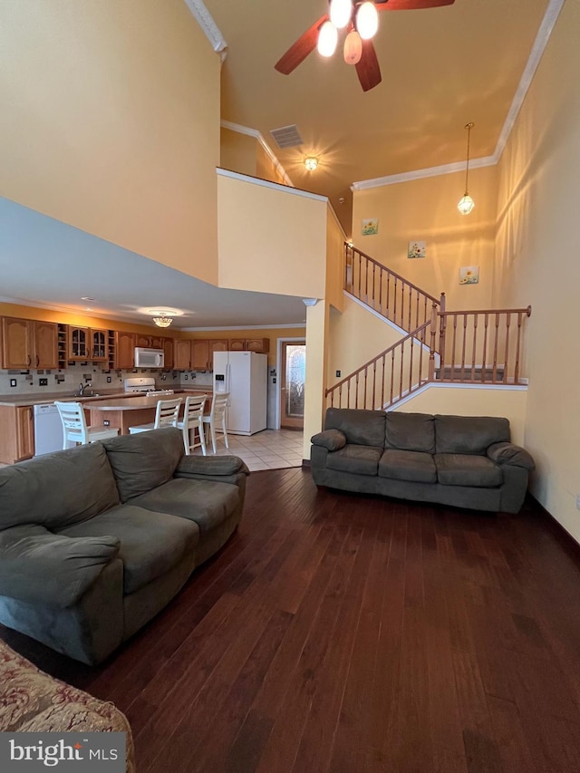 living room with a towering ceiling, ceiling fan, crown molding, sink, and light hardwood / wood-style floors