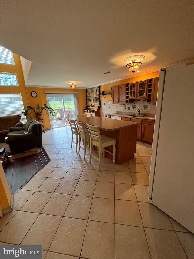 kitchen featuring a center island, backsplash, white refrigerator, sink, and light tile patterned floors