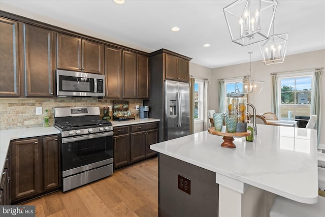 kitchen featuring tasteful backsplash, pendant lighting, light wood-type flooring, and appliances with stainless steel finishes