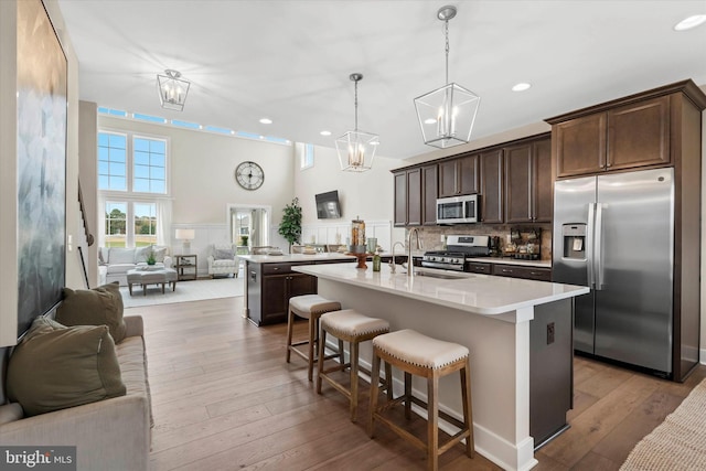 kitchen featuring a kitchen island with sink, hanging light fixtures, sink, light hardwood / wood-style floors, and stainless steel appliances