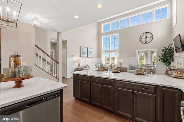 kitchen featuring light stone countertops, an inviting chandelier, stainless steel dishwasher, pendant lighting, and light wood-type flooring