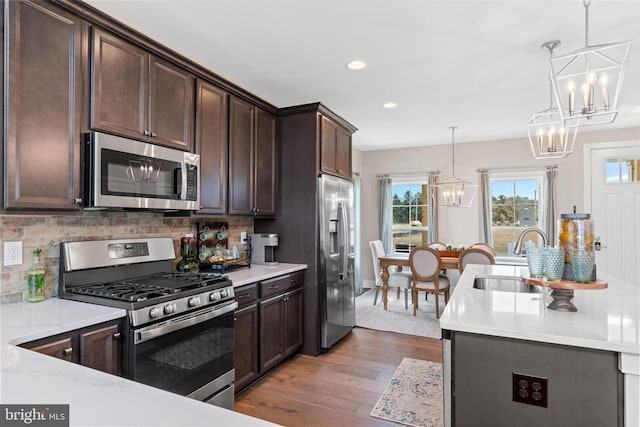 kitchen with sink, decorative light fixtures, light hardwood / wood-style floors, dark brown cabinetry, and stainless steel appliances