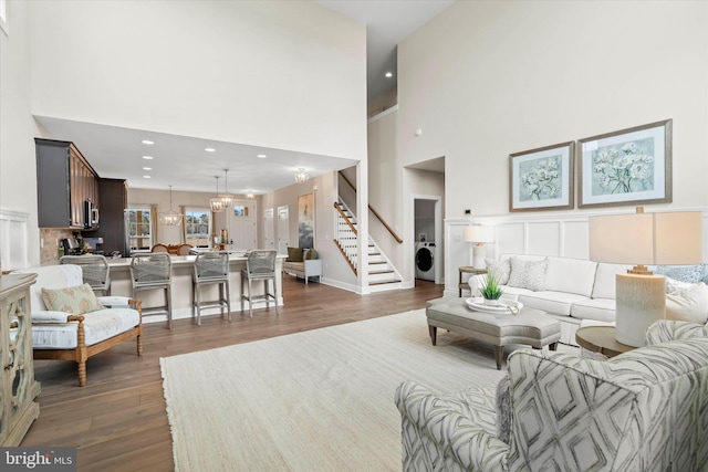 living room featuring washer / clothes dryer, dark hardwood / wood-style floors, a high ceiling, and an inviting chandelier