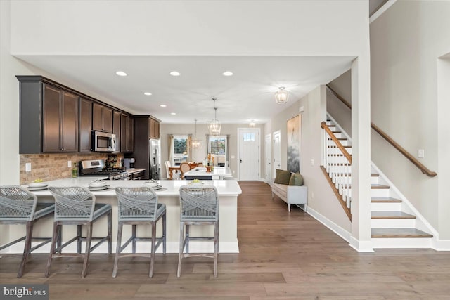 kitchen with a kitchen breakfast bar, appliances with stainless steel finishes, decorative light fixtures, light hardwood / wood-style floors, and kitchen peninsula