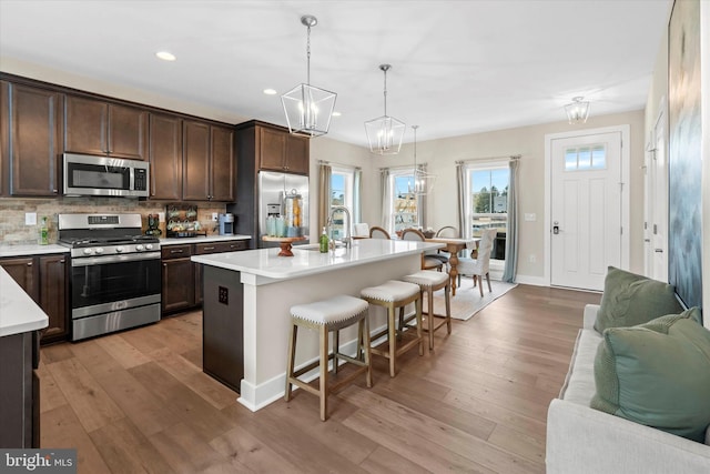 kitchen with a kitchen bar, an island with sink, stainless steel appliances, and light wood-type flooring