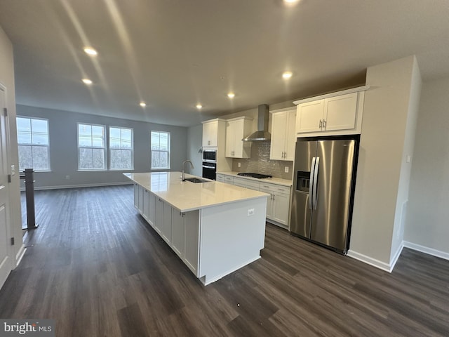 kitchen with dark hardwood / wood-style flooring, wall chimney exhaust hood, stainless steel appliances, white cabinetry, and an island with sink