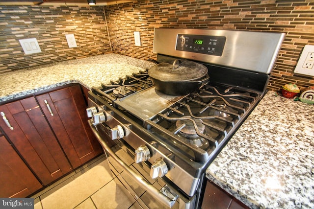 kitchen featuring tile patterned flooring, tasteful backsplash, light stone countertops, and stainless steel range with gas stovetop