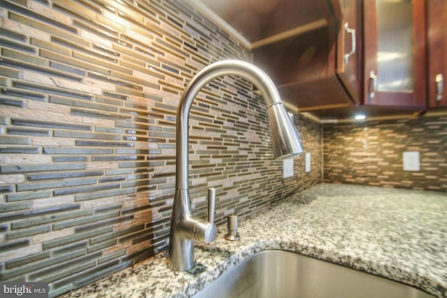 interior details featuring decorative backsplash, light stone counters, and sink