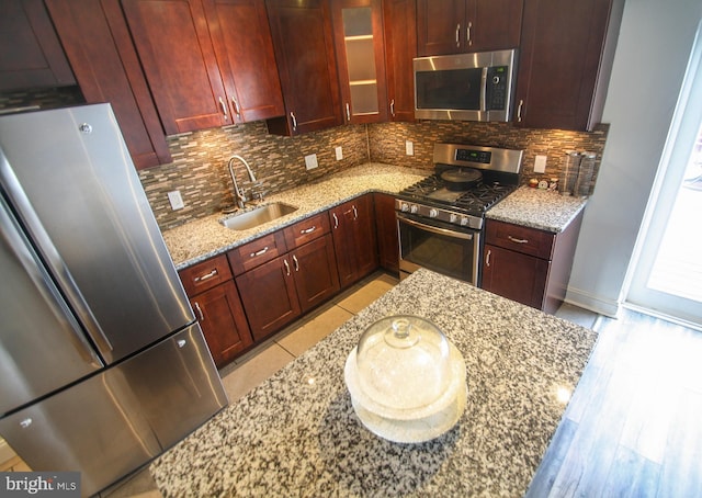 kitchen with light stone countertops, sink, stainless steel appliances, light hardwood / wood-style floors, and decorative backsplash