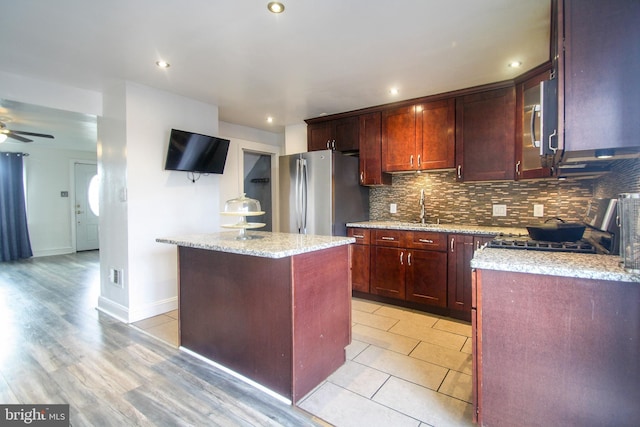 kitchen featuring light stone countertops, a center island, ceiling fan, stainless steel appliances, and light hardwood / wood-style flooring