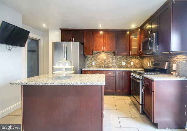 kitchen featuring light stone countertops, decorative backsplash, stainless steel appliances, sink, and a center island