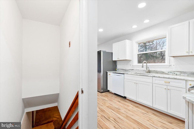 kitchen with white dishwasher, white cabinets, stainless steel refrigerator, and light hardwood / wood-style flooring