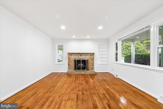 unfurnished living room with a fireplace, built in features, and hardwood / wood-style flooring