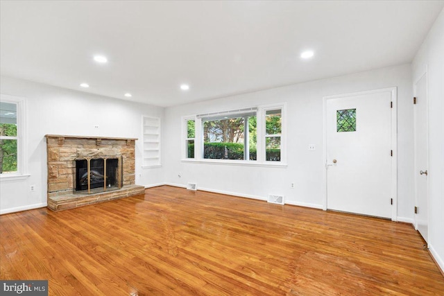 unfurnished living room with a stone fireplace, a wealth of natural light, and light hardwood / wood-style flooring