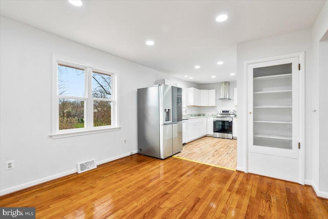 kitchen with white cabinetry, light hardwood / wood-style flooring, stainless steel appliances, and wall chimney range hood