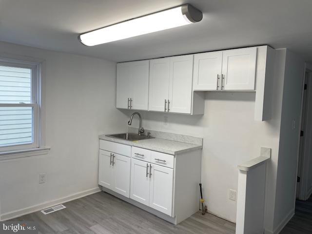 kitchen with white cabinetry, sink, and light hardwood / wood-style flooring