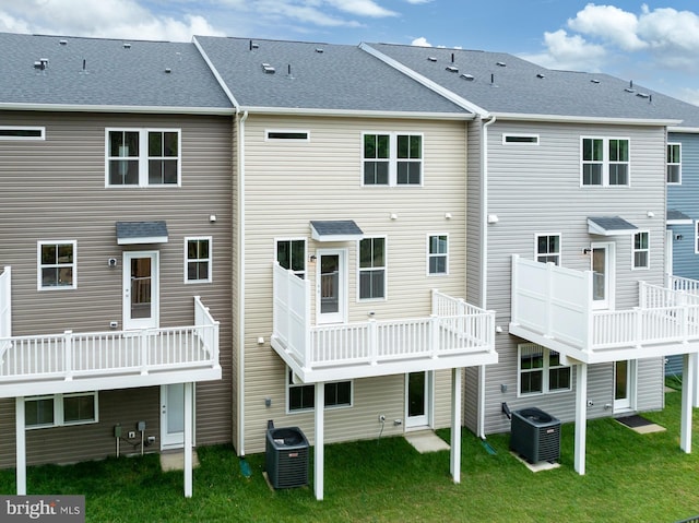 rear view of property featuring central AC unit and a lawn