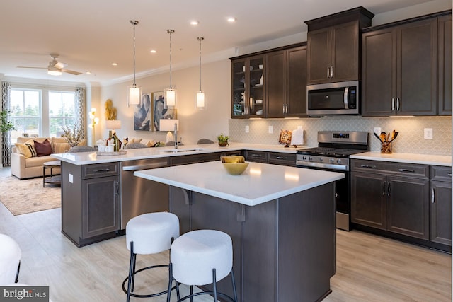 kitchen featuring ceiling fan, stainless steel appliances, a kitchen bar, a kitchen island, and light wood-type flooring